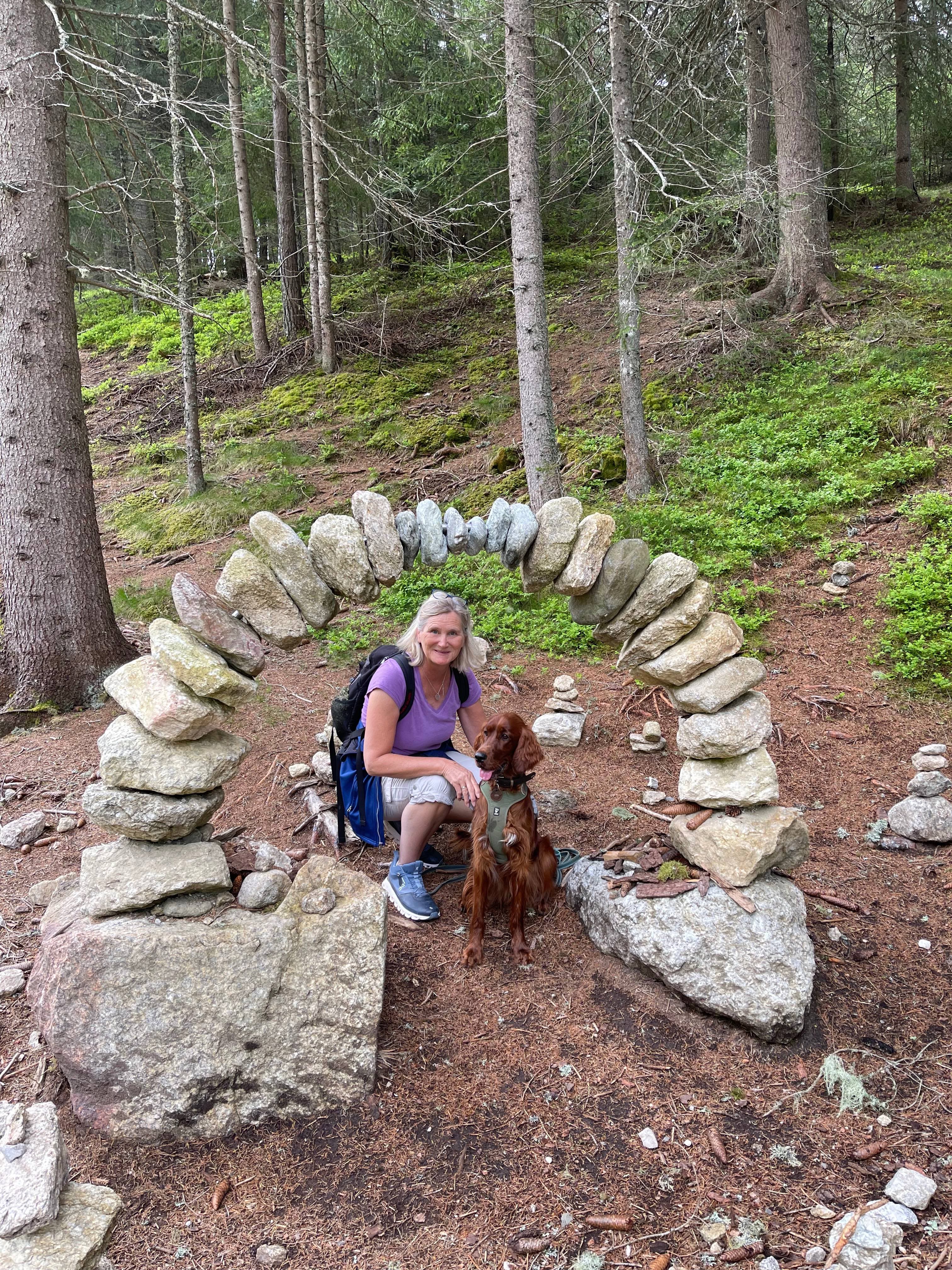 Irish Red Setter mit Besitzerin unter einem dekorativen Steinbogen im grünen Wald